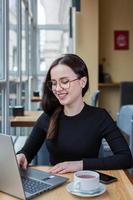 bella mujer de negocios trabajando en una laptop en una cafetería. mujer independiente que se conecta a internet a través de la computadora. blogger o periodista escribiendo un nuevo artículo. foto