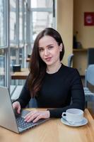 bella mujer de negocios trabajando en una laptop en una cafetería. mujer independiente que se conecta a internet a través de la computadora. blogger o periodista escribiendo un nuevo artículo. foto