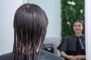 el peluquero aplica una máscara para el cabello al cabello negro liso. cuidado del cabello en el salón de belleza. foto