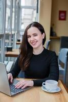 bella mujer de negocios trabajando en una laptop en una cafetería. mujer independiente que se conecta a internet a través de la computadora. blogger o periodista escribiendo un nuevo artículo. foto