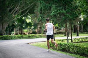 Back side view. Asian man sportsman fit body wearing smart watch while running or jogging in the garden have more tree and clean air, exercising at park. Sport healthy running concept. photo