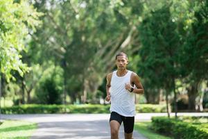 Asian man sportsman fit body wearing smart watch while running or jogging in the garden have more tree and clean air, exercising at park. Sport healthy running concept. photo