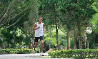 asiático hombre deportista ajuste cuerpo vistiendo inteligente reloj mientras corriendo o trotar en el jardín tener más árbol y limpiar aire, hacer ejercicio a parque. deporte sano corriendo concepto. foto