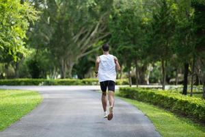 Back side view. Asian man sportsman fit body wearing smart watch while running or jogging in the garden have more tree and clean air, exercising at park. Sport healthy running concept. photo