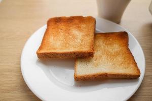 dos piezas de tostado rebanado un pan en un blanco plato y café en de madera mesa, Listo a hacer emparedado para desayuno. selectivo enfocar. foto