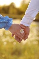 romantic date concept. young man and woman hands holding each other. girl with golden ring on finger in blue dress with chamomile flower in hand photo