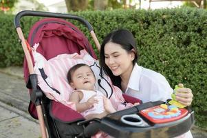 Beautiful mom with a baby girl sitting on baby trolley outdoor in sunshine day photo