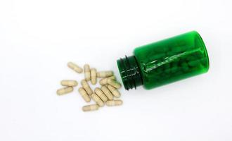 Top view of white pills spill or pour out of green pill bottle isolated on white background with copy space. Healthy, herb, Flat lay container object and Medicine. Food supplement, cure, repair health photo