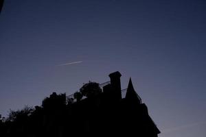 silueta Clásico casas con avión fumar en puesta de sol cielo. foto