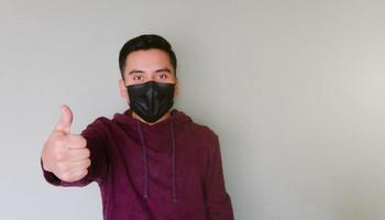 Young man with face mask making thumbs up sign photo