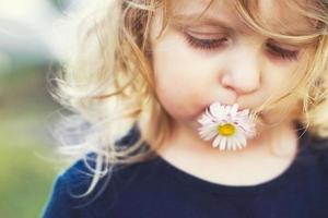 niña con un margarita flor en su boca en un verde antecedentes cerca. labios con flor en césped antecedentes. retrato de un pequeño niña foto