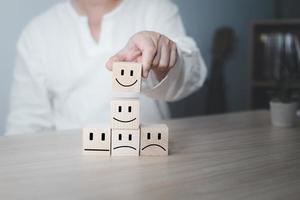 Hand of a businessman chooses a smile face on wood block circle.Customer service experience and business satisfaction survey.rating very impressed.Satisfaction survey concept. photo