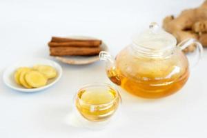 a cup of tea with ginger root, lime, cinnamon and teapot on white background. Health drink concept. photo