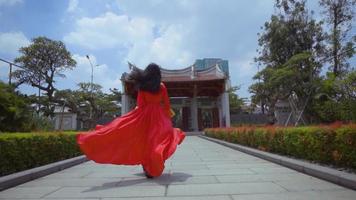 un' bellissimo giovane Cinese donna giocando con un' rosso cheongsam vestito dentro il giardino video