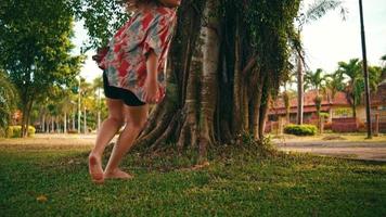 un asiatico donna corse e subito sat giù nel davanti di un' grande ombreggiato albero con verde erba nel un' parco video