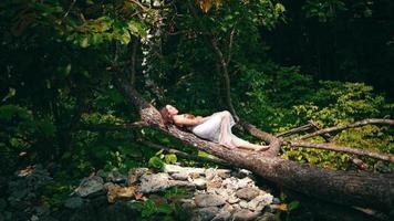 An Asian woman is sleeping on a tree trunk full of green leaves while enjoying the calming island's atmosphere video