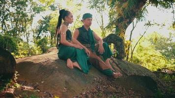 Asian woman and man are sitting on a rock wearing green dresses enjoying the view video