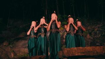 une groupe de asiatique femmes dans vert traditionnel vêtements portant bambou masques ensemble tandis que permanent parmi le rochers video