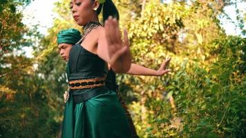 an asian woman and man dancing together while wearing green traditional clothes in the middle of the forest early video
