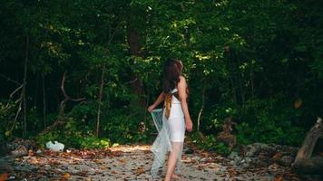 un asiático mujer en blanco ropa camina dentro un tropical bosque con un montón de sombreado arboles en un hermosa isla video