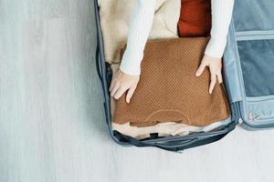 Woman hand packing her winter clothes in luggage. Time to travel, trip, Relax, spring or autumn or winter season and vacation concepts photo