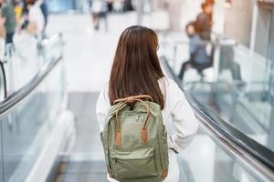 Asian woman traveler with backpack walking on escalator  in international airport. time to Travel, Vacation, trip and Transport concept photo