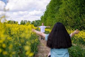 A cute boy in a white T-shirt runs to his mother in a rapeseed field photo