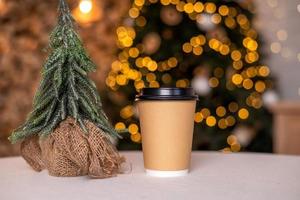 A disposable coffee cup with a lid on the background of a Christmas tree. Place for advertising photo