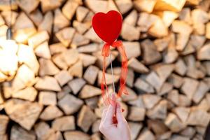 A red heart on a stick is held by a woman's hand photo