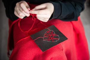 Hands make a card with a heart for Valentine's Day with red threads photo