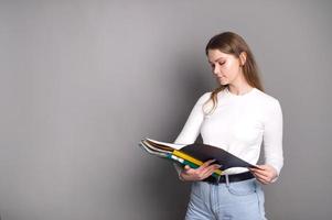 un linda estudiante niña mira dentro un abierto carpeta para documentos y soportes en un gris antecedentes foto