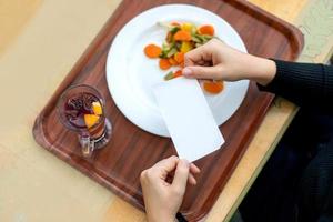 Women's hands hold the receipt over a tray with a plate and fruit tea. photo