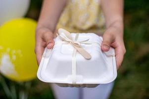 A white box with a ribbon and a wooden spoon for a bento cake in your hands photo