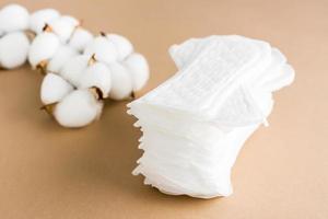 A stack of clean disposable sanitary pads and a branch of cotton on a beige background. Women's health and comfort concept photo