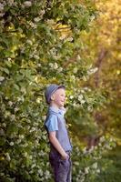 A cute boy is standing in the woods wearing a hat with a brim and smiling photo
