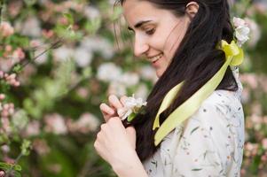 A young woman ties a bow on her hair with a yellow ribbon in a blooming garden photo