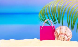 Pink bag for shopping or gift with conch on white sand, behind sea with palm tree. Concept of rest, travel, shopping, holiday in hot country. Copy space photo