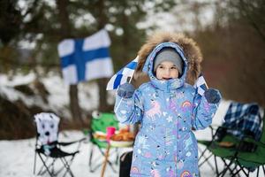 finlandés pequeño niña con Finlandia banderas en un bonito invierno día. nórdico escandinavo gente. foto