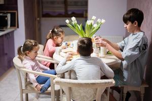 Children eat fruits and desserts, drink tea at home in the evening kitchen. Chocolate on a stick for melting. photo