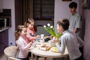 Children eat fruits and desserts, drink tea at home in the evening kitchen. photo