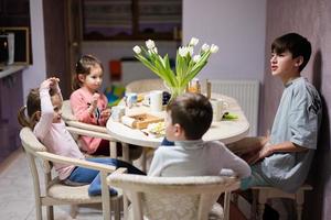 niños comer frutas y postres, bebida té a hogar en el noche cocina. foto