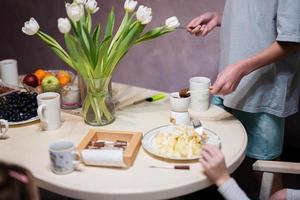 Children eat fruits and desserts, drink tea at home in the evening kitchen. Chocolate on a stick for melting. photo