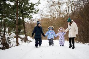 Mother with three kids holding hands and walking in winter forest. photo