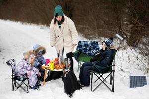 Young woman with children in winter forest on a picnic. Mother and three kids. photo