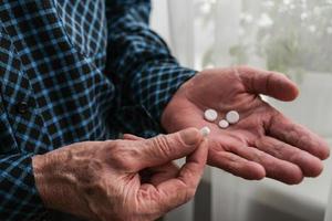 Close-up of an elderly man's hands with pills. The concept of retirement life. The morning of an elderly person begins with taking pills and nutritional supplements. photo