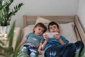 dos pequeño hermanos felizmente acecho dibujos animados juntos en un teléfono inteligente niños y artilugio concepto foto