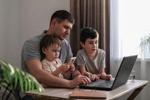 A man works at home with a laptop and looks after the kids. Father freelancer try to work at home with children. Home office and parenting at the same time photo