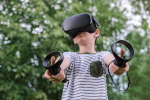 A seven-year-old boy in virtual reality glasses plays outside in the park. Children using technology. selective focus photo