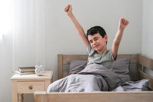 Cheerful boy stretches after waking up in bed. Morning of the schoolboy photo