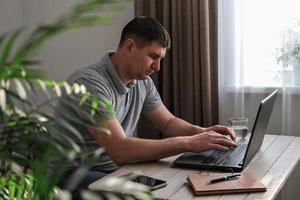 grave joven masculino programador trabajos en un ordenador portátil en un acogedor hogar ambiente. Internet negocio, Lanza libre foto